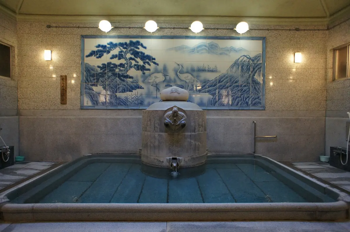可見藍色陶板畫與石造湯釜的道後溫泉本館「神之湯」浴場