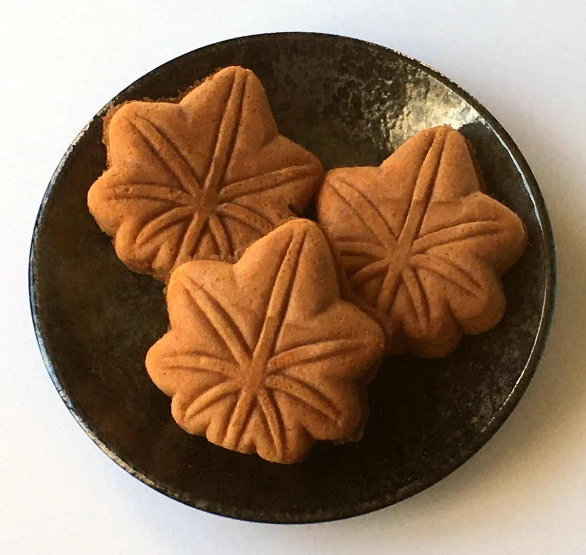 Three maple-leaf-shaped momiji manju on a dark plate