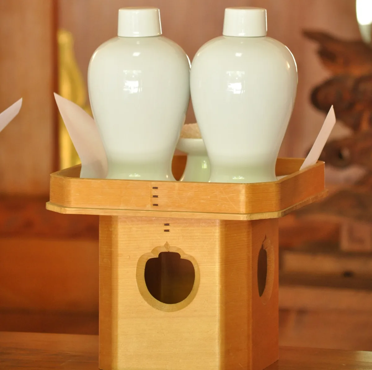 A pair of white ceramic sake bottles offered on a wooden stand (sanpo)